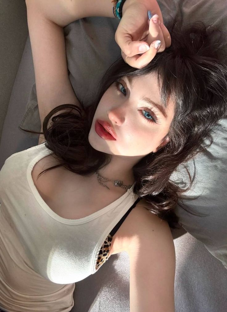 This may contain: a woman laying on top of a bed wearing a white shirt and blue eyeshadow