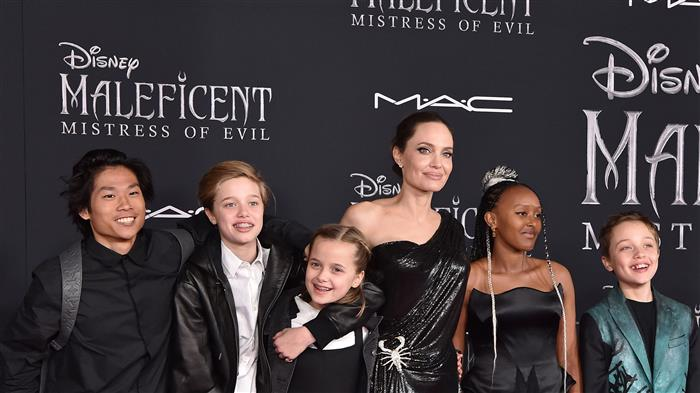 A group of children and a woman dressed in elegant attire pose on the red carpet for the premiere of 'Maleficent: Mistress of Evil'.